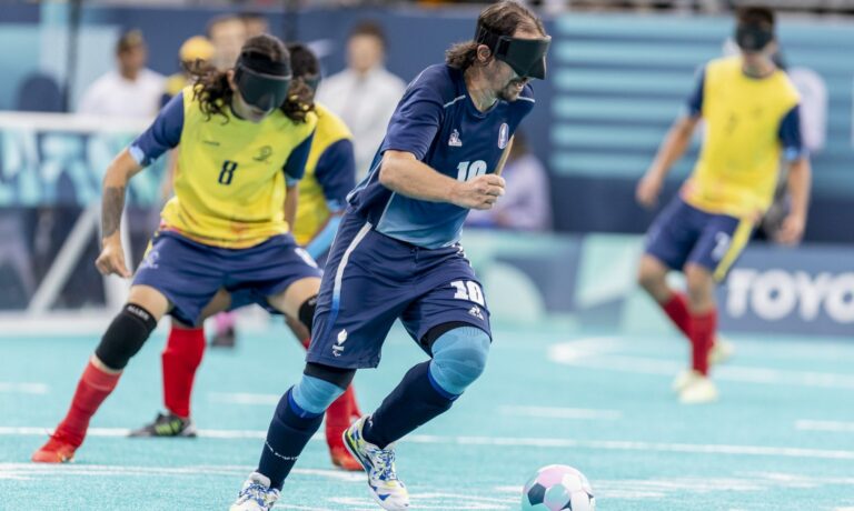 Joueur de l’équipe de France de football pour aveugles en action lors d’un match officiel, portant un bandeau opaque et contrôlant le ballon avec précision sur un terrain indoor.